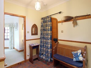 Una habitación con un banco de madera, una mesita pequeña, una cortina estampada, una escoba y un espejo.