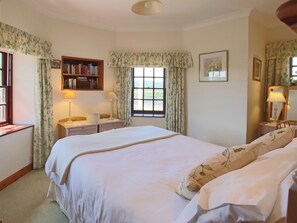 A bedroom with a large bed, a bedside table with a lamp, a bookshelf, and a window with curtains. - CONHEATH GATELODGE COTTAGE (Glencaple, Dumfries)