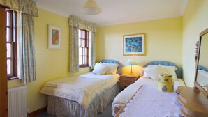A bedroom with two single beds, a bedside table with a lamp, a radiator, and a window with curtains.