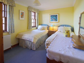 Un dormitorio con dos camas individuales, una mesita de noche con lámpara, un radiador y una ventana con cortinas.