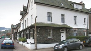 A two-story building with a white facade and a green roof, featuring a stone base. - Ideal family accommodation enjoying fine mountian views from most rooms. (Keswick)