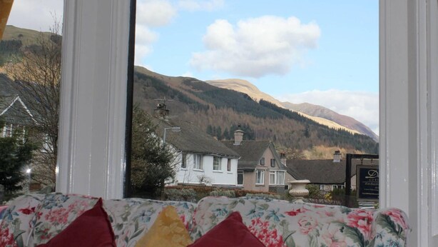A window view of a mountainous landscape with a white building and a signboard. - Ideal family accommodation enjoying fine mountian views from most rooms. (Keswick)