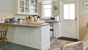 A kitchen with a central island, white cabinets, a microwave, and a clock on the wall. - Ideal family accommodation enjoying fine mountian views from most rooms. (Keswick)