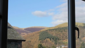 A view from a window overlooking a valley with houses and a stone building. - Ideal family accommodation enjoying fine mountian views from most rooms. (Keswick)