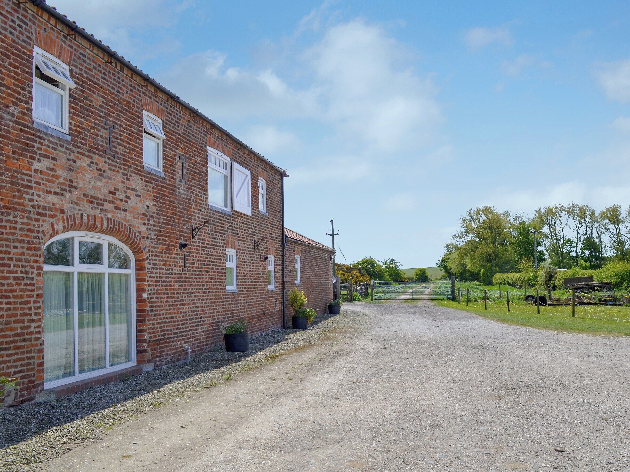 A brick building with a gravel driveway leading to a gated area.