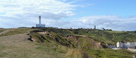 A lighthouse on a grassy hill with a clear sky.