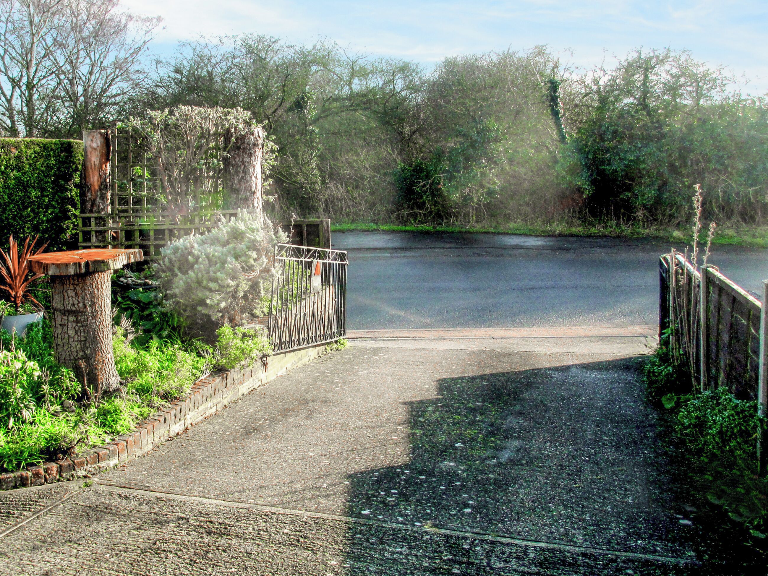 A rustic wooden bridge leading to a road, surrounded by lush greenery and trees.