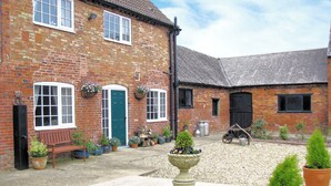 A brick building with a green door, a bench, and potted plants in the courtyard.