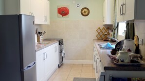 A kitchen with white cabinets, a black refrigerator, a stove, and a sink. There is a clock and a poppy flower on the wall.