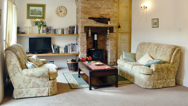 A cozy living room with two floral-patterned armchairs, a wooden coffee table, a bookshelf, a fireplace, and a television.