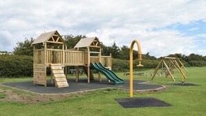 A wooden playground with a slide and climbing wall, surrounded by grass and trees. - 2 bedroom accommodation in Freshwater (Freshwater)