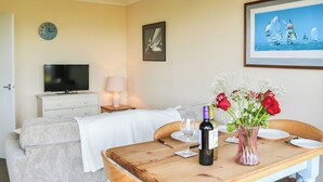 A hotel room with a bed, a TV, a dining table with chairs, a vase with flowers, and a framed picture on the wall. - 2 bedroom accommodation in Freshwater (Freshwater)