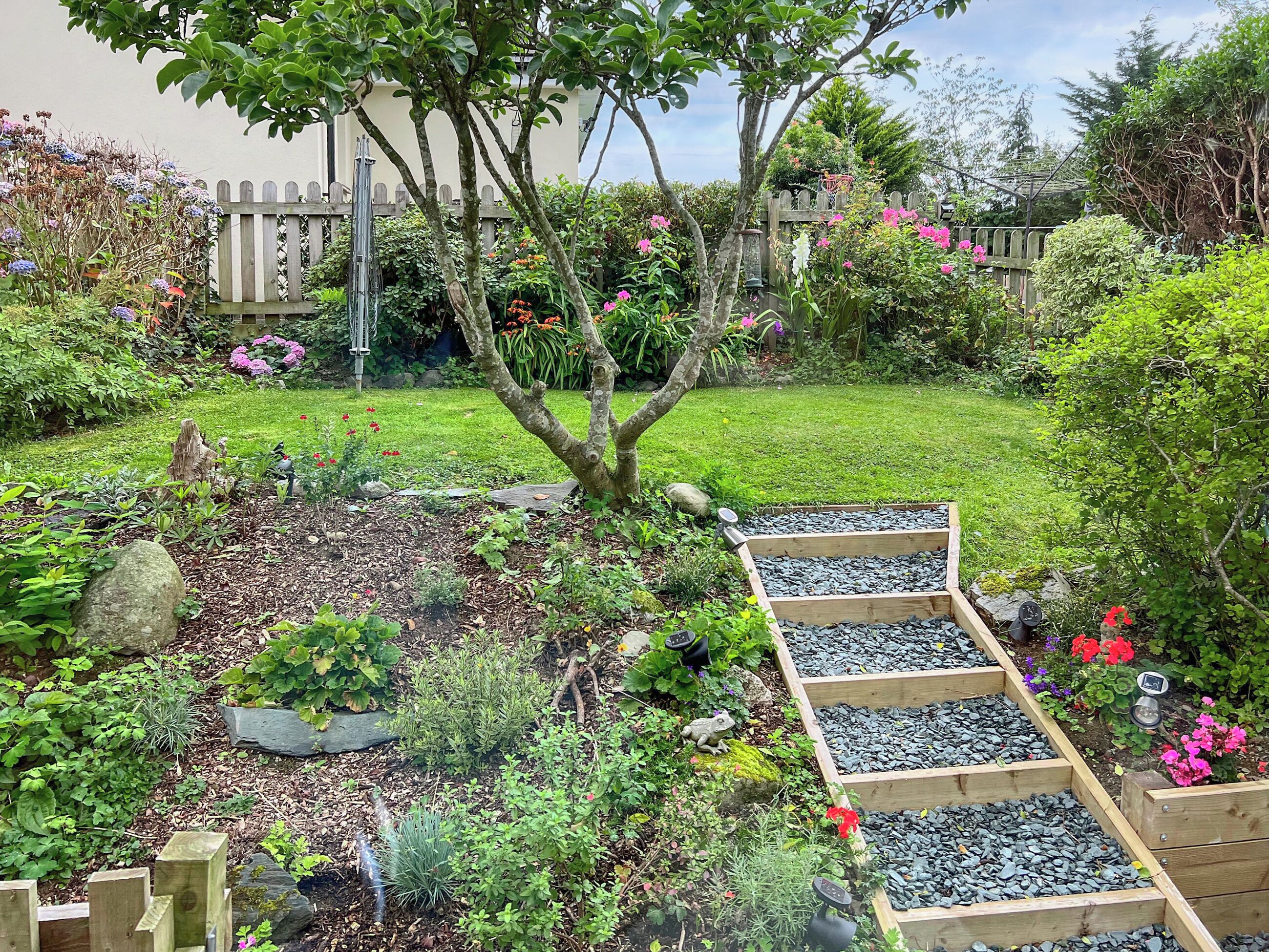 A garden with raised beds, a wooden fence, and a variety of plants and flowers.