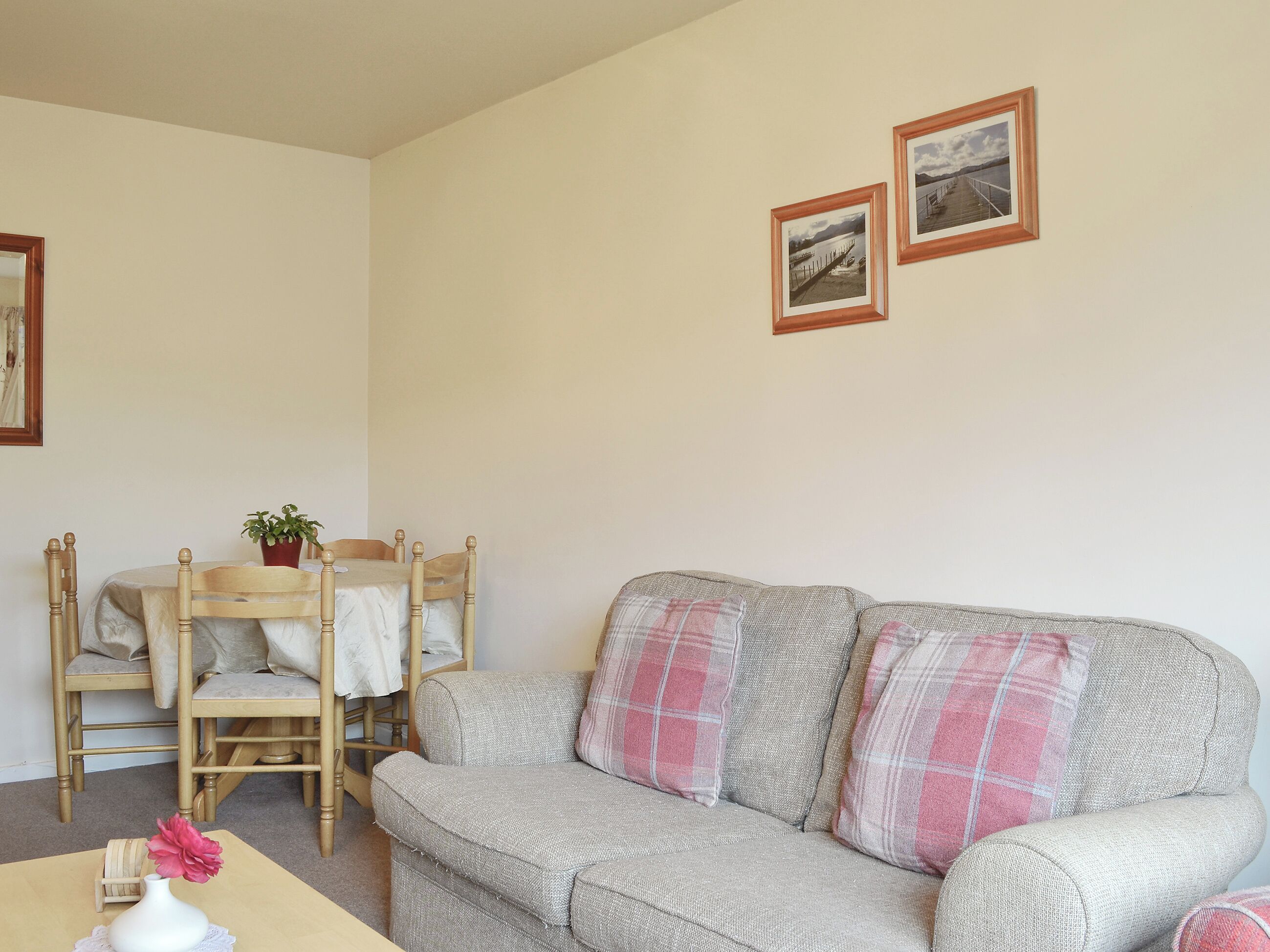 Un salon chaleureux avec un canapé gris, des chaises en bois, une petite table sur laquelle est posé un vase, et deux tableaux encadrés accrochés au mur.