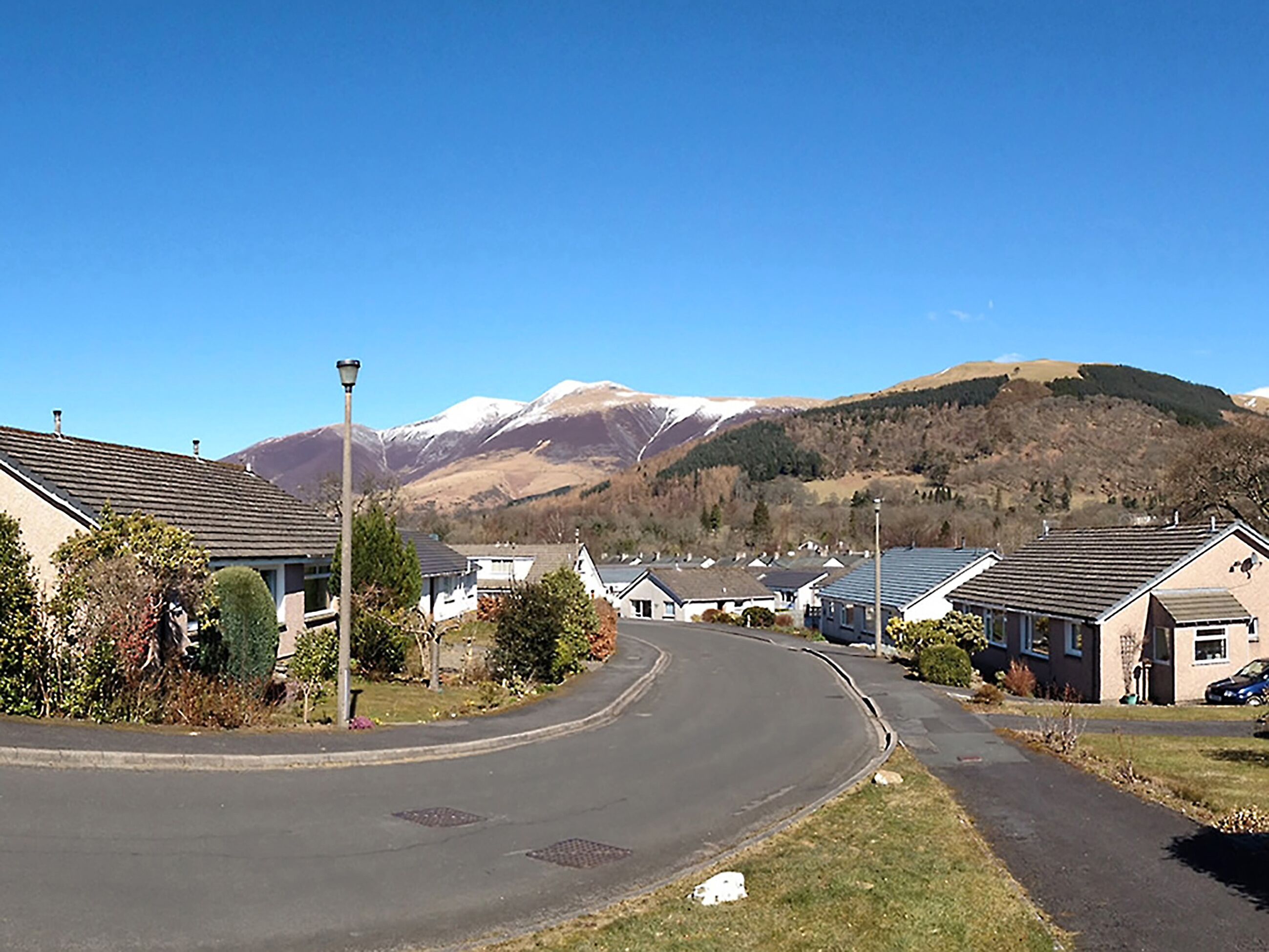 A residential street with houses, a curved road, and a mountain range in the background.