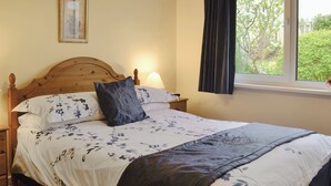A neatly made bed with floral bedding, a wooden headboard, and a nightstand with a lamp.