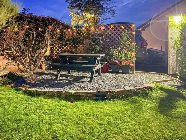 A garden patio with a wooden bench, surrounded by gravel, with potted plants and a lattice fence. - 2 bedroom accommodation in Keswick (Keswick)