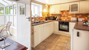 A kitchen with white cabinets, a black oven, a microwave, and a toaster. There is a window with a view of greenery outside. - 2 bedroom accommodation in Docking, near Hunstanton (Docking, near Hunstanton)