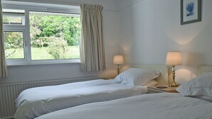 Ein Schlafzimmer mit zwei Betten, einem Fenster mit Vorhängen, einem Heizkörper und zwei Nachttischlampen.