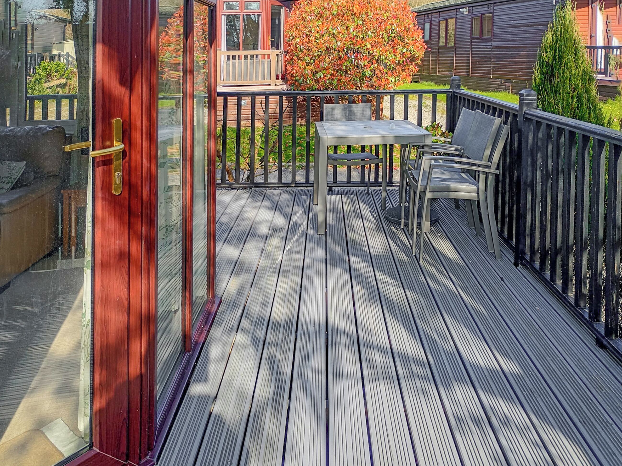 A wooden deck with a table and chairs, a red door, and a view of a house and tree.