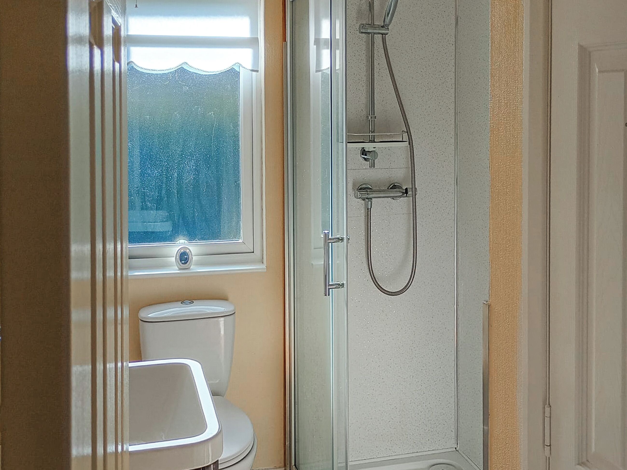 A bathroom with a glass shower enclosure, a toilet, and a window with frosted glass.