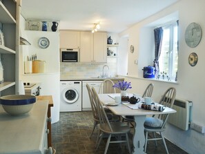Une cuisine compacte comprenant un coin repas, un lave-linge, un four à micro-ondes et une fenêtre avec des rideaux.