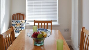A dining table with a fruit bowl, two chairs, and a window with blinds. - 1 bedroom accommodation in Filey (Filey)