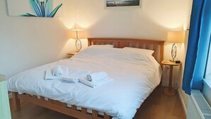 A neatly made bed with white linens and towels, two bedside lamps, a framed picture on the wall, and a window with blue curtains. - 1 bedroom accommodation in Filey (Filey)
