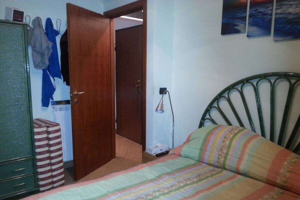 A bedroom with a bed, a wardrobe, a door, and a wall-mounted lamp.