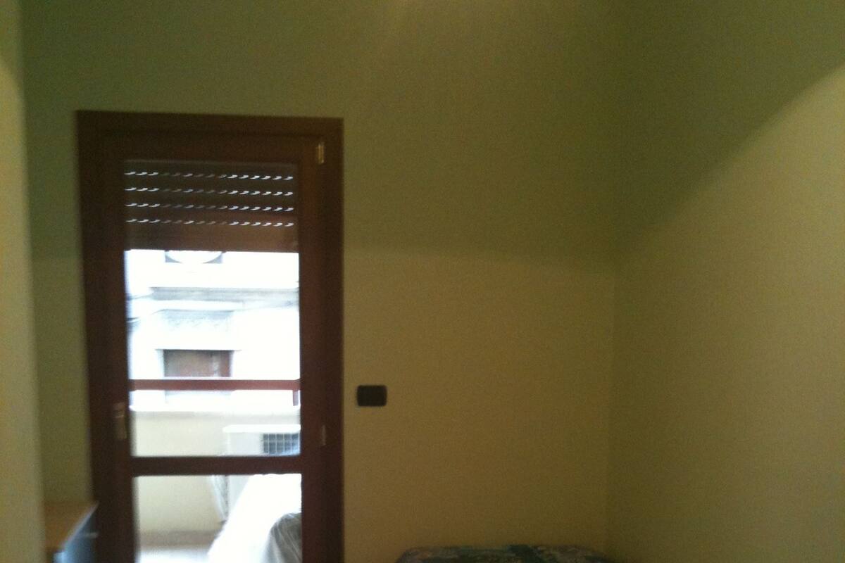 A small room with a bed, a nightstand, and a door leading to a balcony.