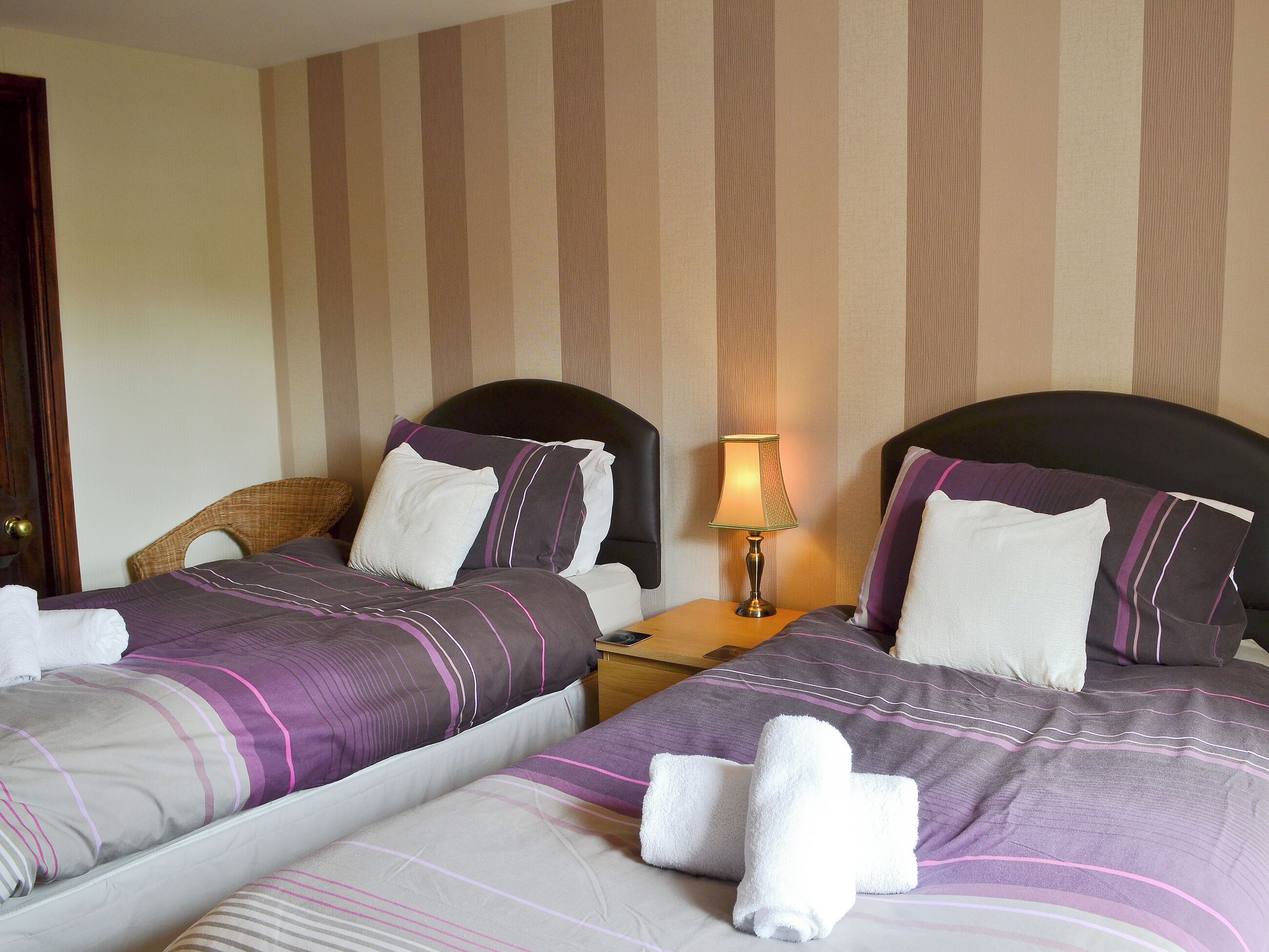 Une chambre d’hôtel avec deux lits, une literie à rayures, une table de chevet avec une lampe et un mur à rayures.