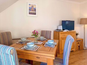 A dining area with a wooden table set for four, striped chairs, a vase with flowers, and a framed picture on the wall.