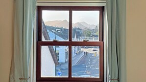 Une fenêtre donnant sur une rue et des montagnes.