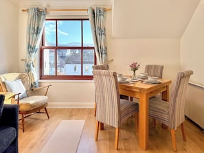 A dining area with a wooden table and striped chairs, a window with curtains, and a view of buildings outside.