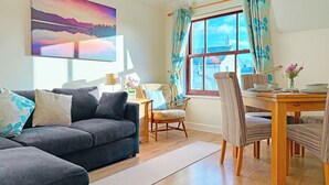 Un salon avec un canapé, une table à manger et des chaises, une fenêtre avec des rideaux et un tableau accroché au mur.