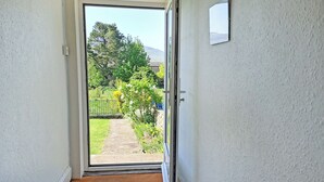 Ein Durchgang zu einem Garten mit einem Steinweg, einem Metallgitter und freiem Blick auf Bäume und eine ferne Hügelkette.