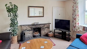Ein Wohnzimmer mit Kamin, Fernseher, Couchtisch, Sofa und einem Blumentopf.