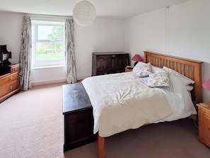 A bedroom with a bed, a dresser, a nightstand, a lamp, and a window with curtains. - 2 bedroom accommodation in Sedbusk, near Hawes (Sedbusk, near Hawes)