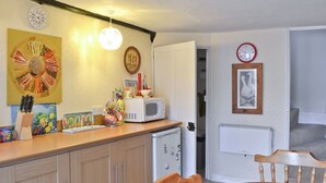 A compact kitchen with a microwave, a small refrigerator, and a dining table with chairs. There are clocks on the wall and a door leading to another room. - 3 bedroom accommodation in Lympstone, near Exmouth (Lympstone, near Exmouth)