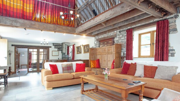 A spacious living room with a large sofa set, a wooden coffee table, and a stone fireplace. A staircase with a wooden railing leads to an upper level. - 3 bedroom accommodation in Bleadon, near Weston-super-Mare (Bleadon, near Weston-super-Mare)