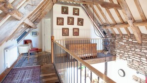 A rustic attic room with exposed wooden beams, a stone wall, and a wooden staircase. - 3 bedroom accommodation in Bleadon, near Weston-super-Mare (Bleadon, near Weston-super-Mare)