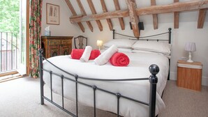 A bedroom with a bed, wooden beams, a window with curtains, a bedside table, and a lamp. - 3 bedroom accommodation in Bleadon, near Weston-super-Mare (Bleadon, near Weston-super-Mare)