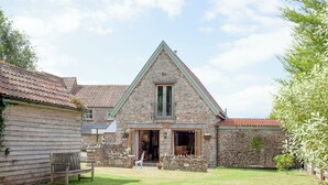A stone house with a triangular roof, a wooden bench, and a grassy yard. - 3 bedroom accommodation in Bleadon, near Weston-super-Mare (Bleadon, near Weston-super-Mare)
