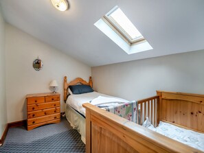 A bedroom with a skylight, a wooden bed, a nightstand, a dresser, and a crib.