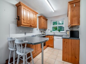 A kitchen with wooden cabinets, a granite countertop, a built-in dishwasher, and a window with a view of greenery.