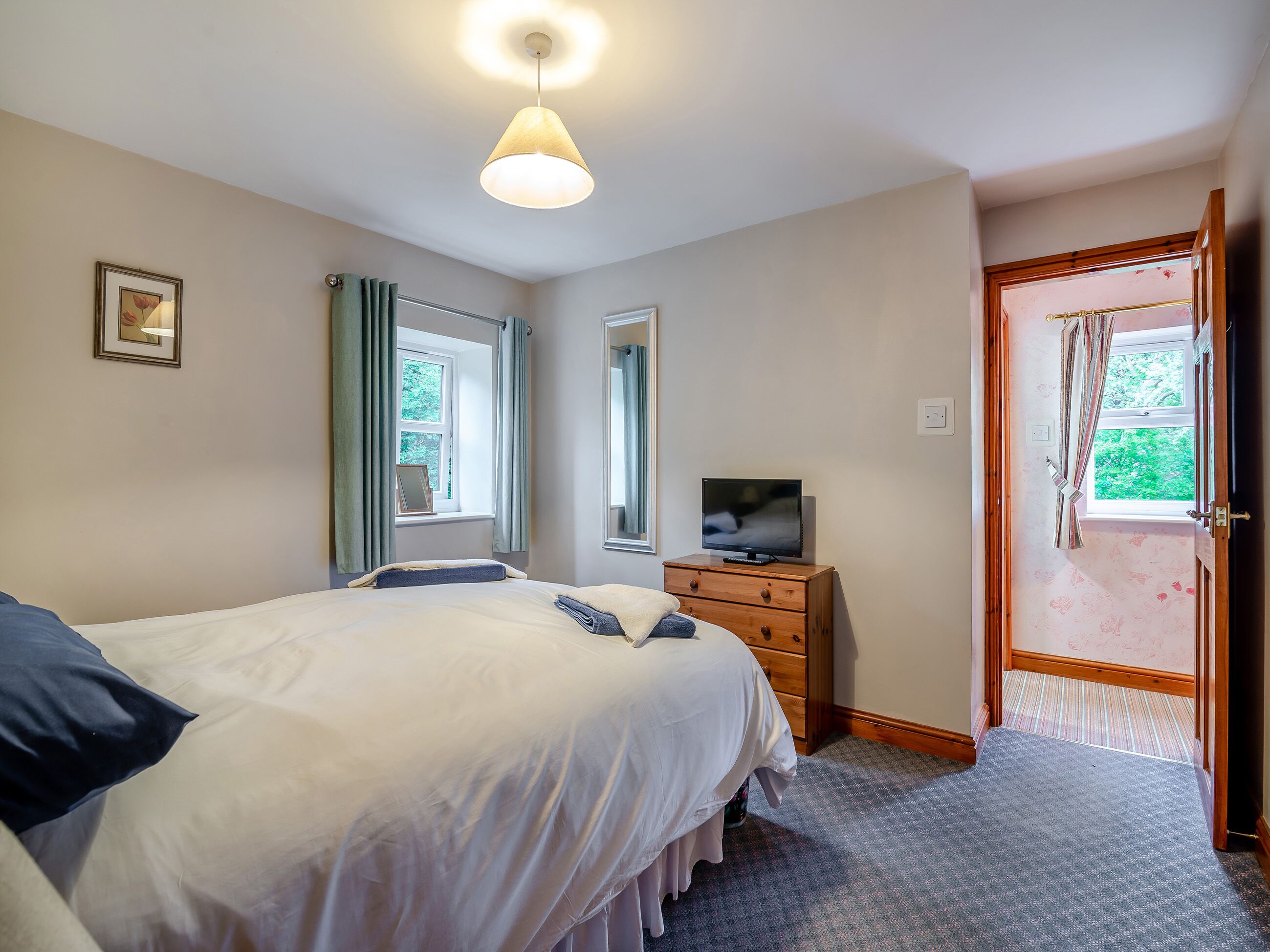 Une chambre à coucher comprenant un lit, une commode, un téléviseur et une porte donnant sur un balcon.