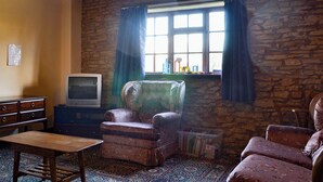 Ein Zimmer mit einer Steinwand, einem Holztisch, einem alten Sessel und einem Fernseher.