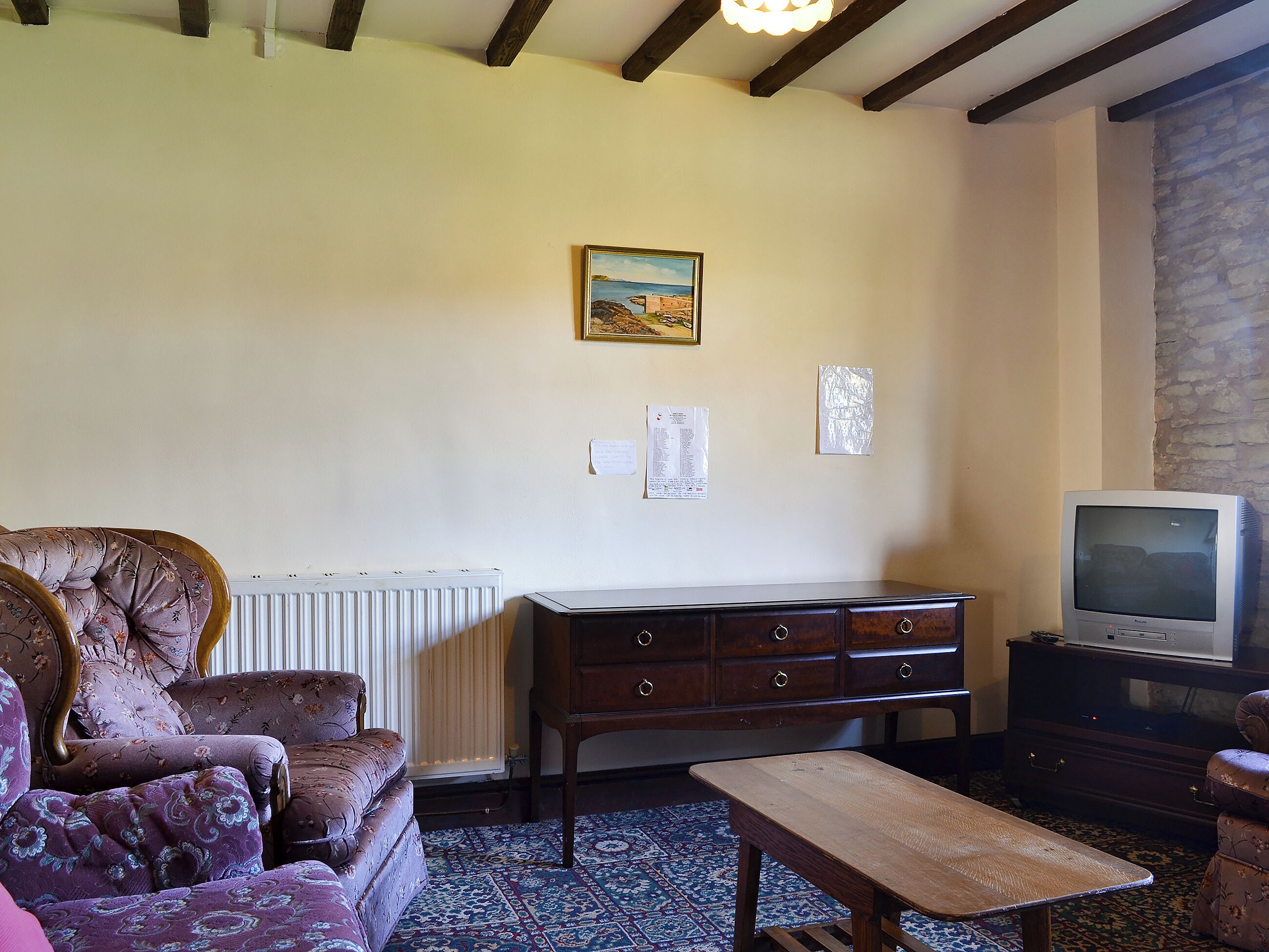 A living room with a sofa, a wooden coffee table, a television, a radiator, and a patterned rug.