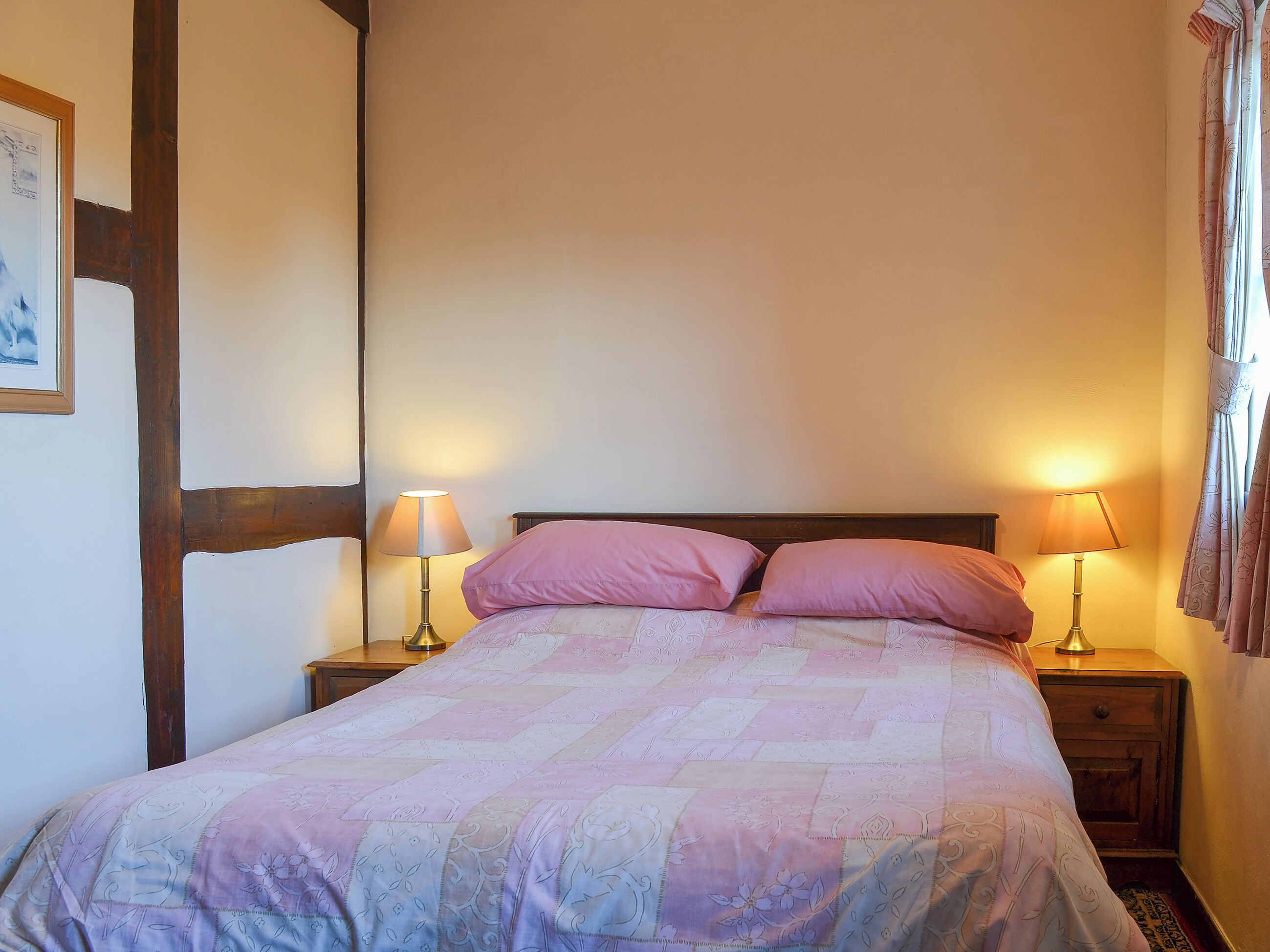 A bed with a floral quilt, two bedside lamps, and a wooden headboard in a room with plain walls.