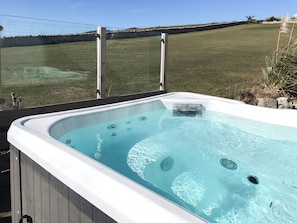 Un bain à remous offrant une vue dégagée sur un champ verdoyant et un mur de pierre en arrière-plan.